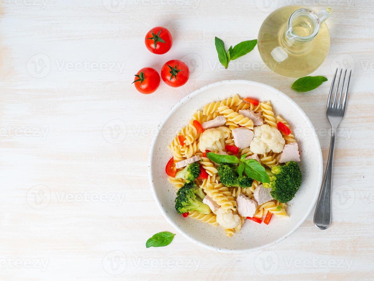 Pasta fusilli with vegetables, turkey meat on white wooden table, low-calorie diet, low-fat food, top view, copy space photo