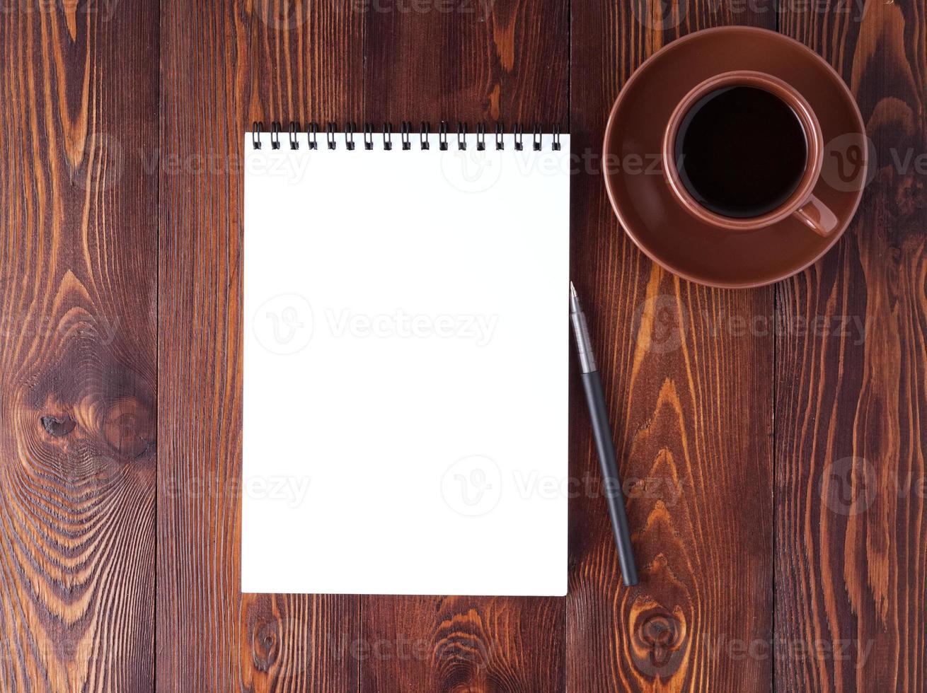 open notepad with spiral, pen and coffee cup on dark brown wooden table, top view photo