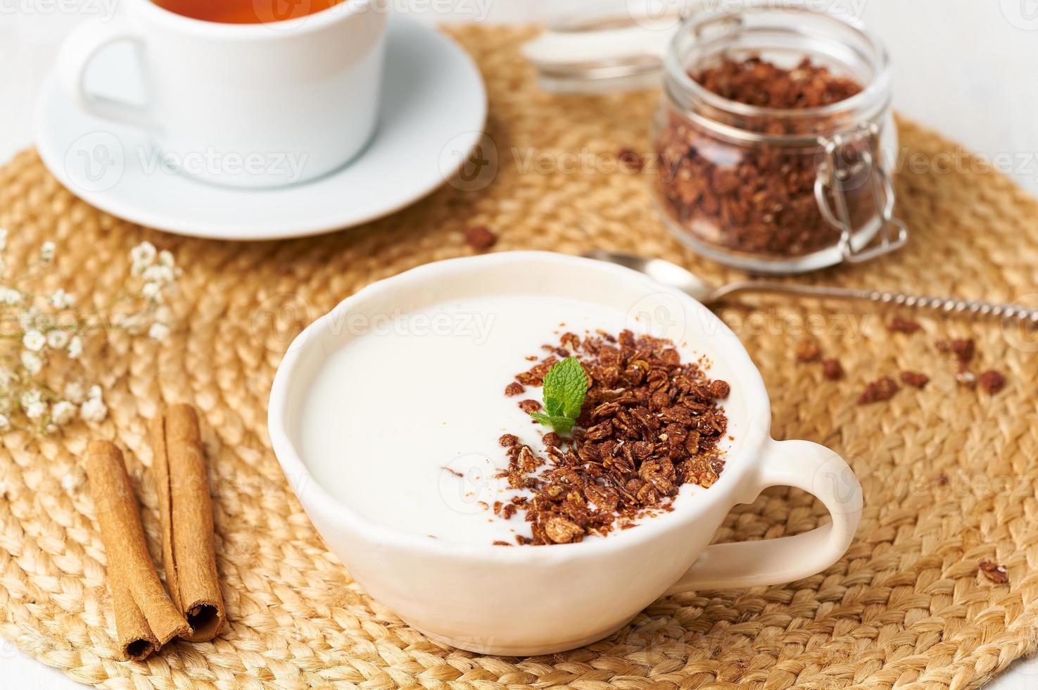 yogur con granola de chocolate en taza, desayuno con té sobre fondo beige, vista lateral. foto