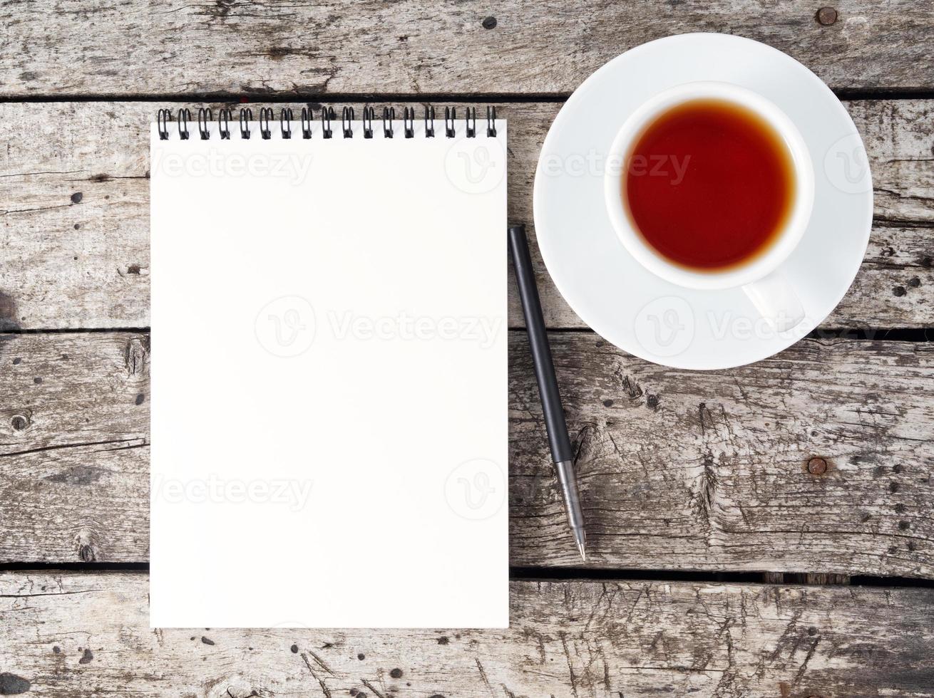 libreta abierta con página blanca limpia, bolígrafo y taza de café en una mesa de madera rústica antigua, vista superior foto