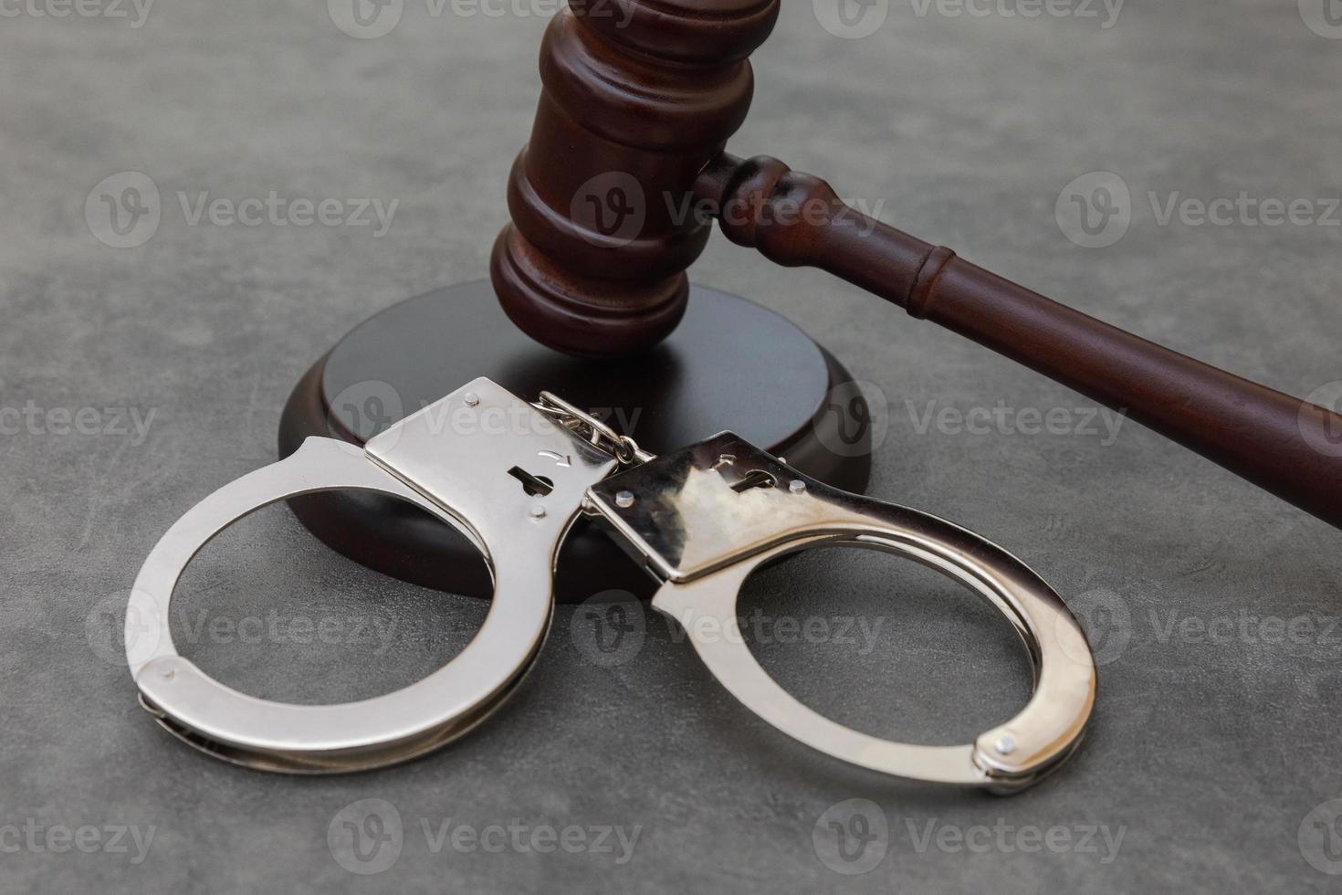 Law theme. Court of law trial in session. Judge gavel handcuffs on grey table in lawyer office or court session. Mallet of judge on concrete stone grey background. Justice human rights concept. photo