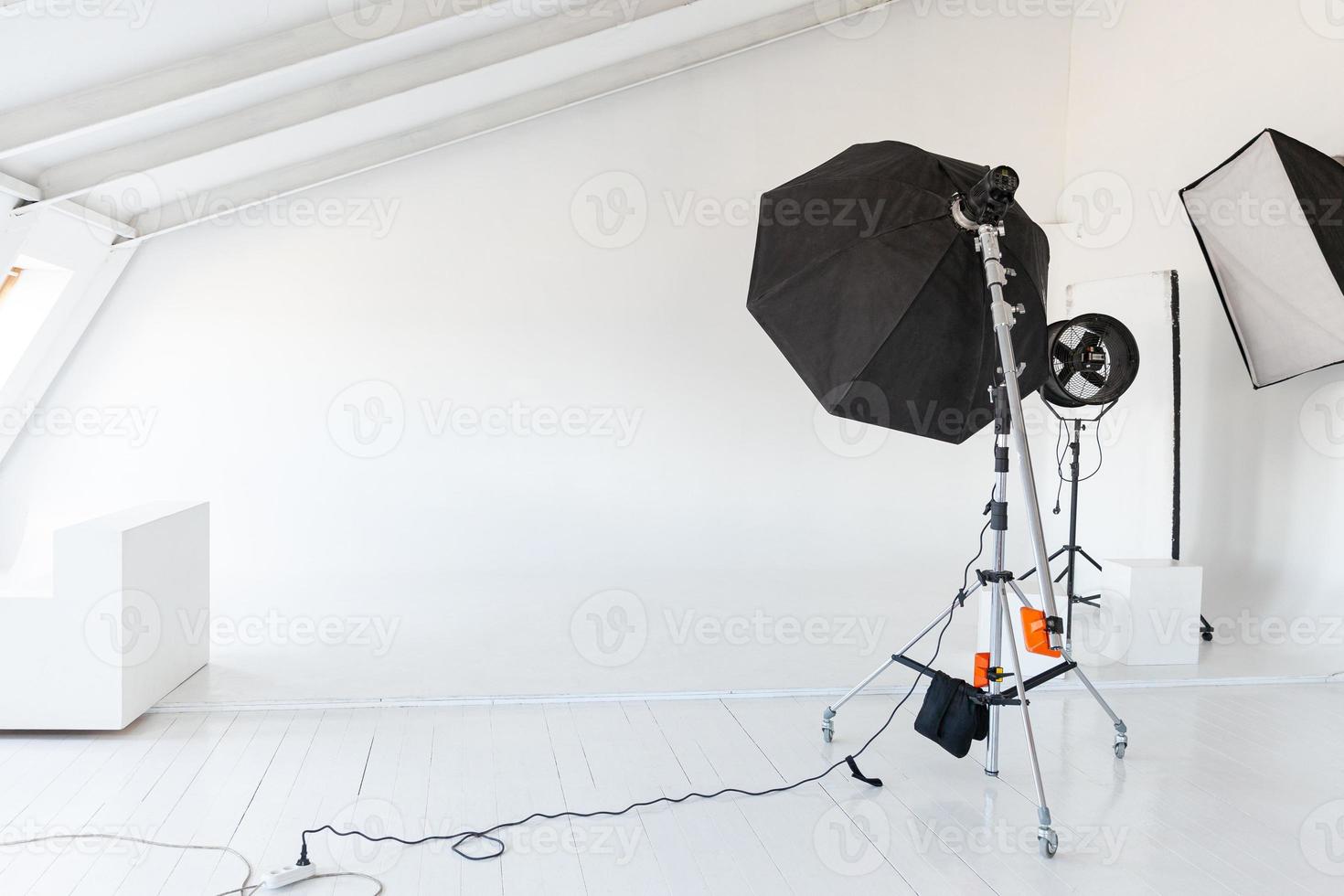 estudio fotográfico vacío con equipo de iluminación. interior del lugar de trabajo del fotógrafo con equipo de herramientas profesionales. escenas de fondo blanco con luz de flash listas para disparar en estudio. estudio de fotógrafo moderno foto