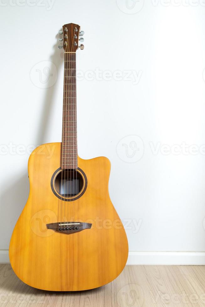 una guitarra acústica acorazada apoyada contra el fondo de la pared blanca. espacio de copia de imagen veritcal. foto