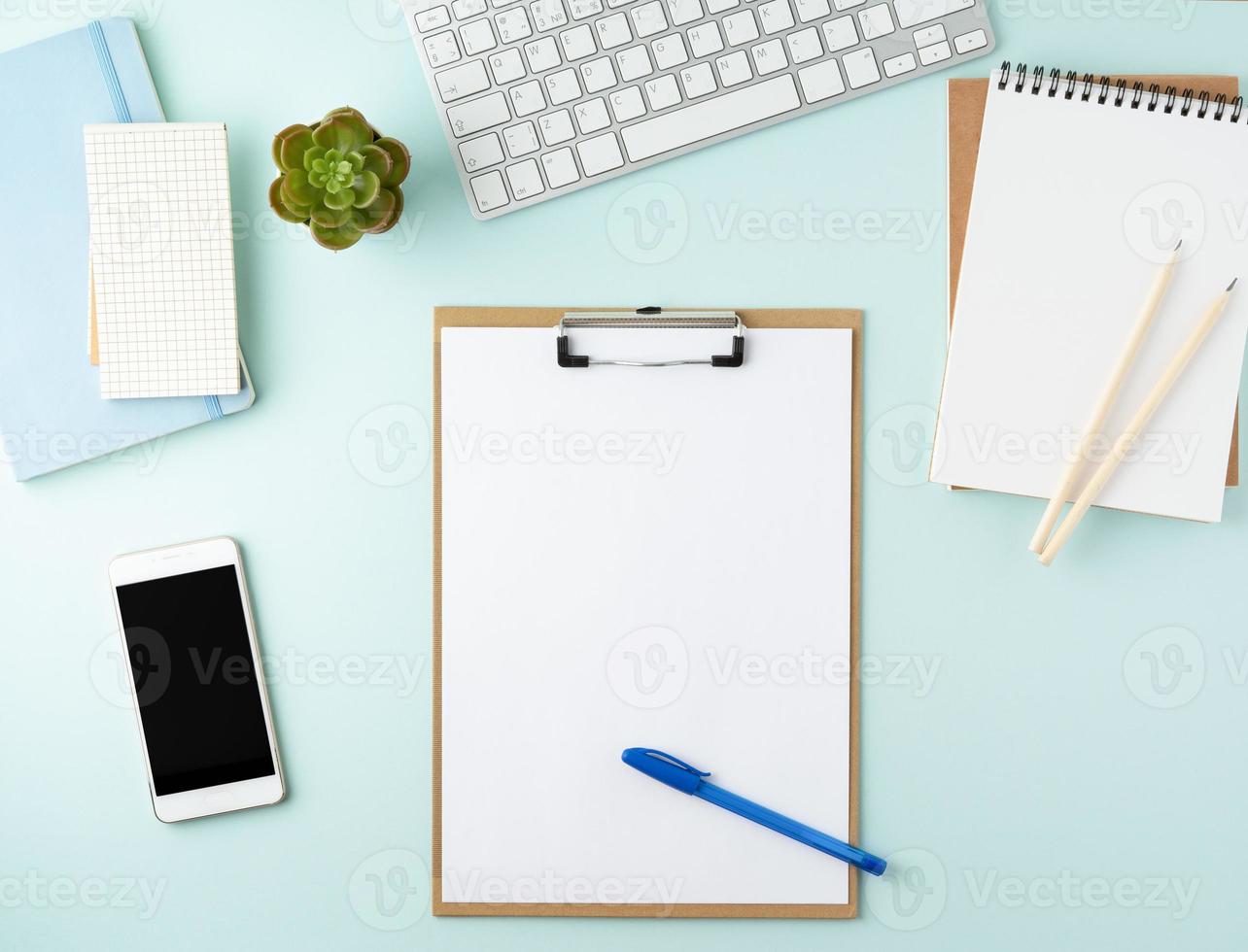 Top view of modern blue office desktop with blank notepad, computer, smartphone. Mock up, photo