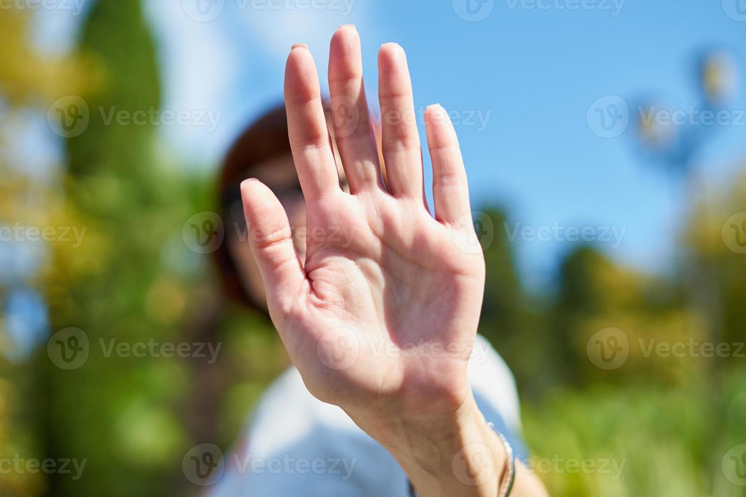 Unrecognizable woman shielding her face from camera. Concept of privacy, personal space, prohibition of photography. Female on blue sky, summer sunny day. Stop, taking pictures is forbidden photo
