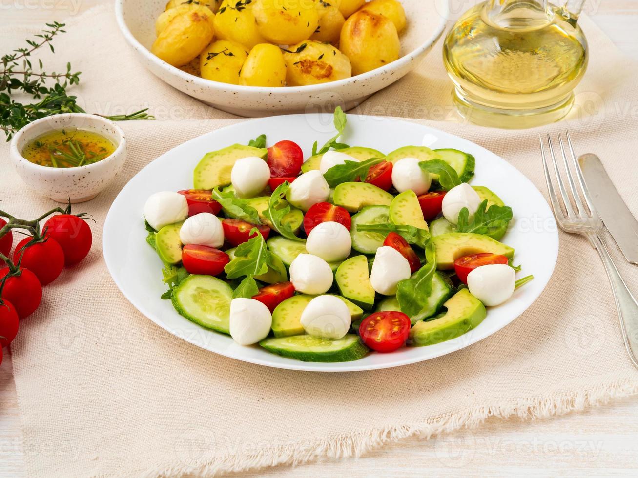 Fresh salad with tomatoes cucumbers arugula mozzarella and avocado. Oil with spices, baked potatoes, side view close up photo