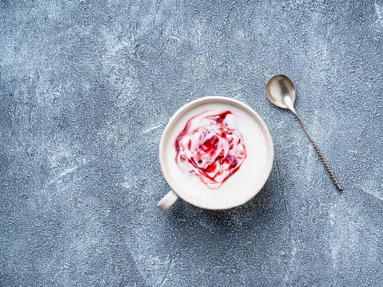 Greek yogurt with jam in white bowl on grey blue concrete stone table, top view, copy space photo