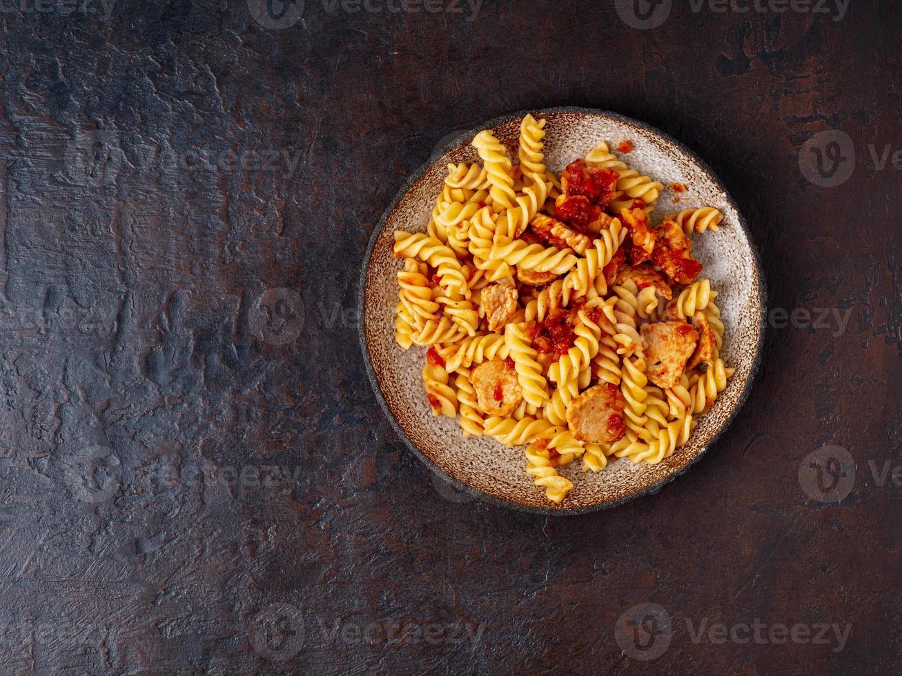 fusilli pasta with tomato sauce, chicken fillet on dark stone concrete background, cope space, top view photo