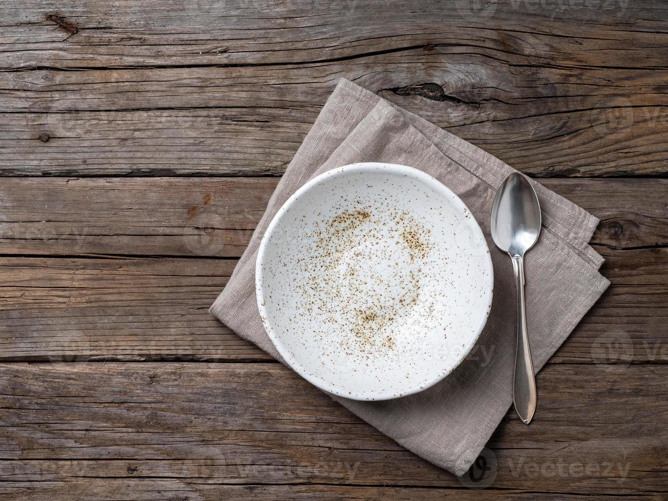 empty soup plate and spoon on rustic gray wooden table, linen napkin, top view photo