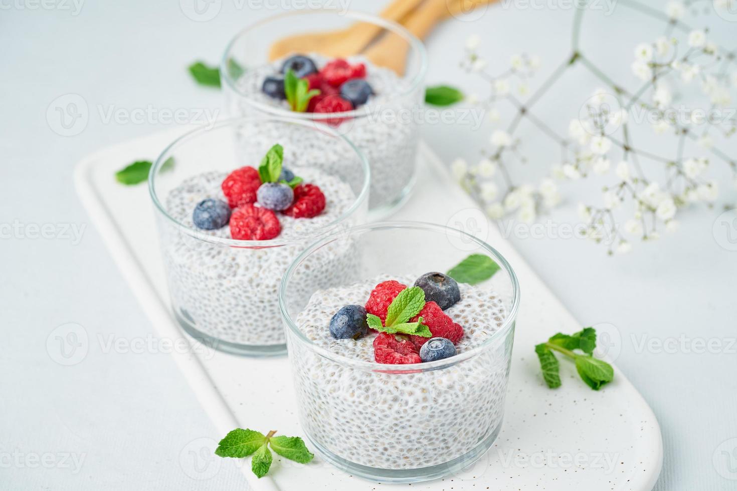 Chia pudding with fresh berries raspberries, blueberries. Three glass, light background, side view, flowers. photo