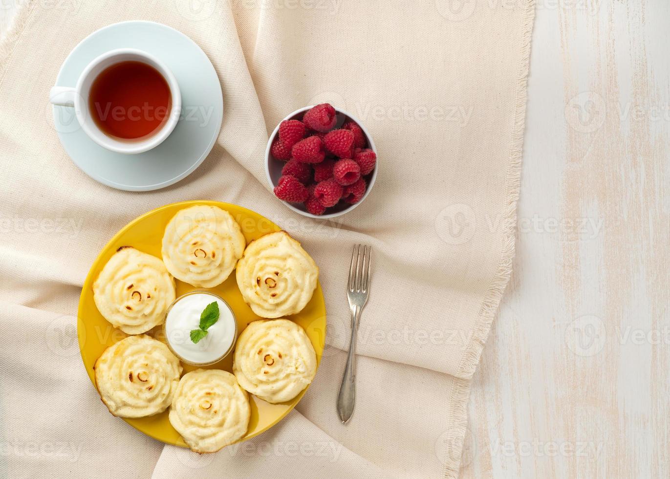 Diet cheese pancakes, rose shape, on yellow plate with tea, raspberry on textile linen napkin photo