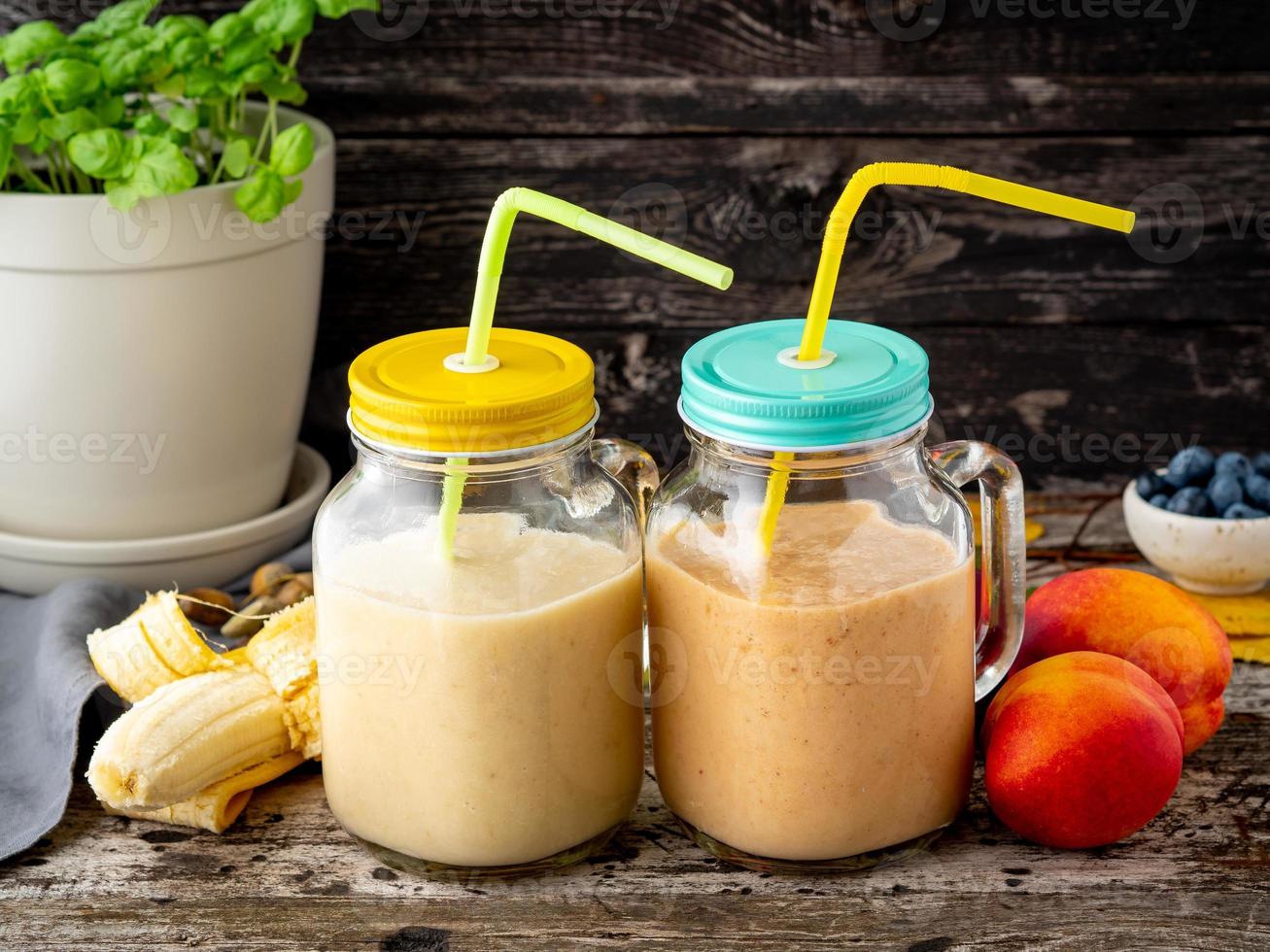 banana peach nectarine smoothie in two jars, fresh fruit milkshakes on old dark rustic wooden table, side view photo