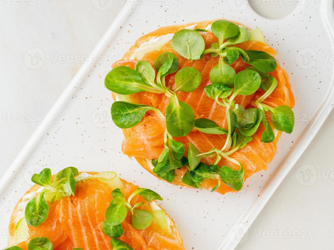 Two open sandwiches with salmon, cream cheese, cucumber slices on white marble table photo