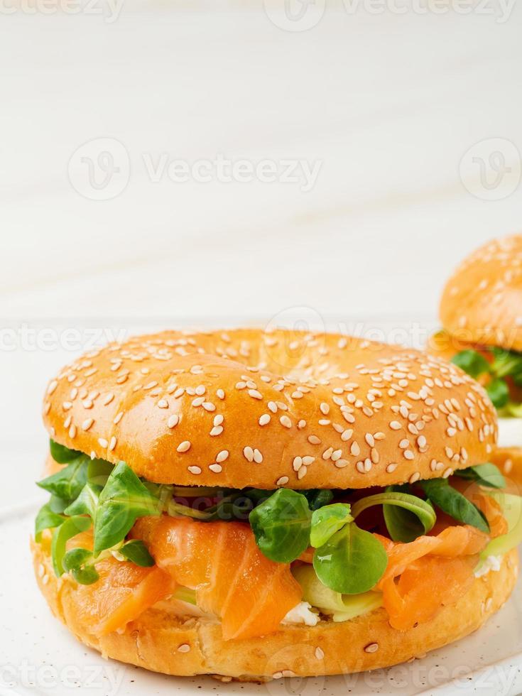 Two sandwiches with salmon, cream cheese, cucumber slices on white marble table, vertical, copy space photo