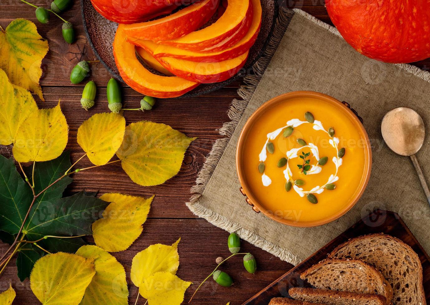 Autumn food. Pumpkin puree soup, leaves, dark brown old wooden table, top view. photo