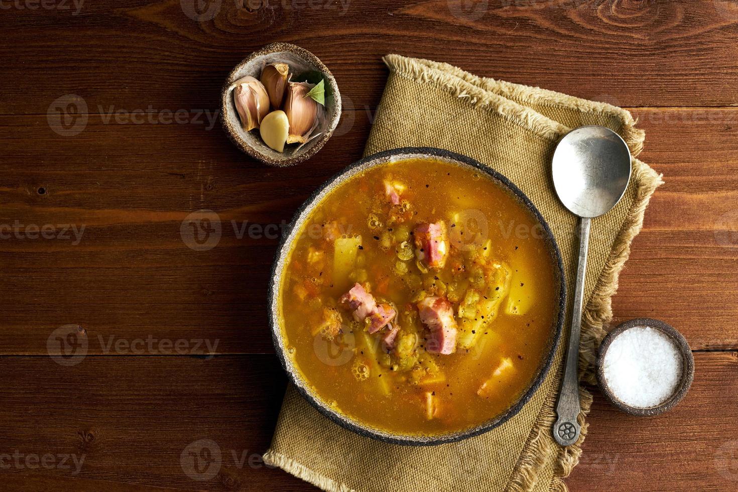 Winter hot soup with chopped green peas, pork, bacon, smoked on dark brown wooden table. Delicious appetizing fat rich soup. photo
