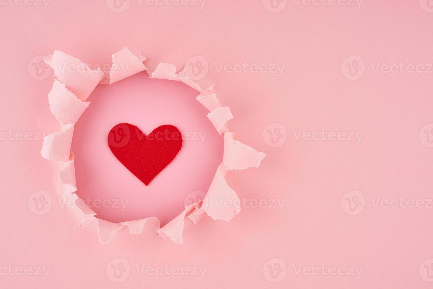 Valentine's Day. A ripped hole and red heart in bright pink textured background, concept of rupted paper with copy space. Long width side banner photo