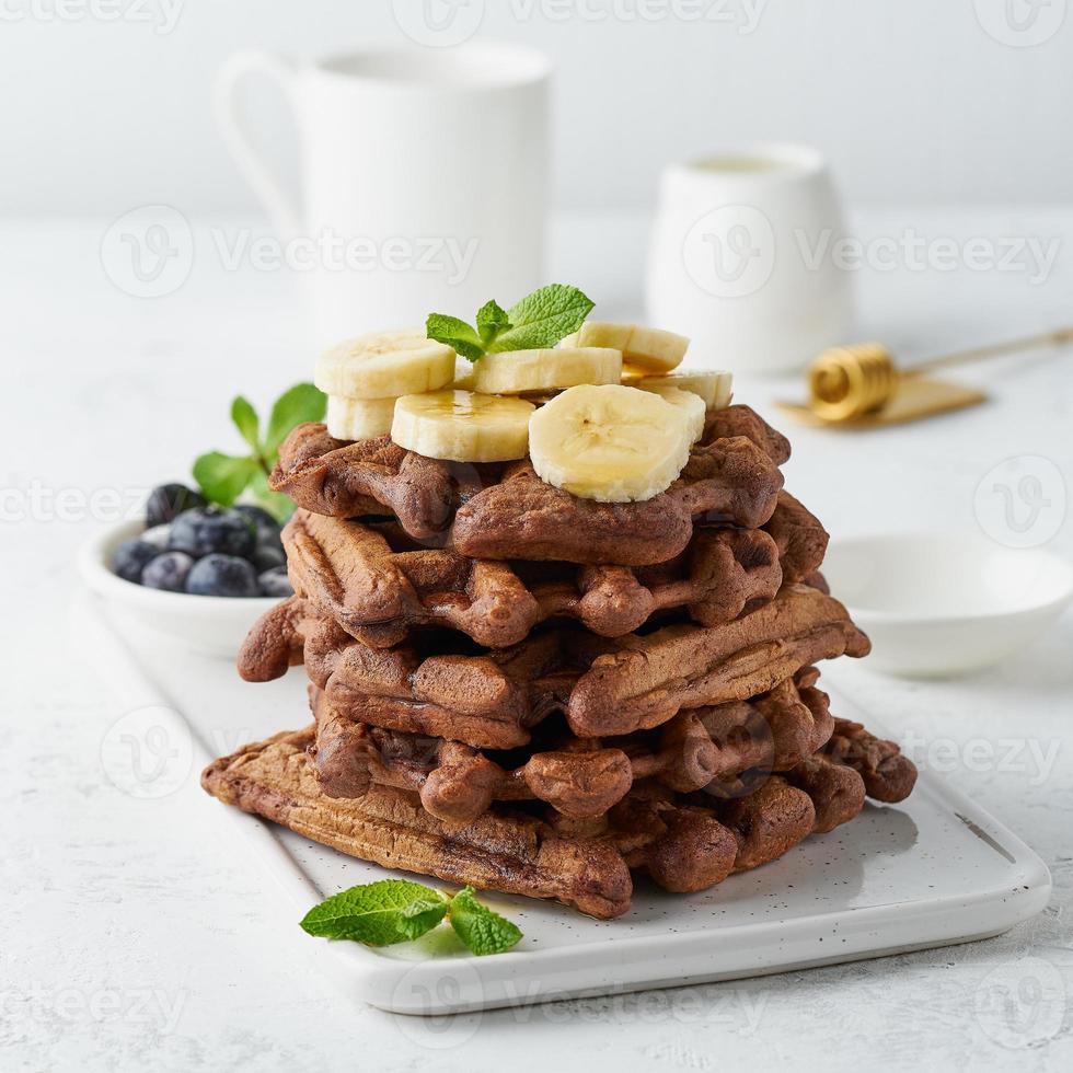 Chocolate banana waffles with maple syrup on white table, close up, side view. photo