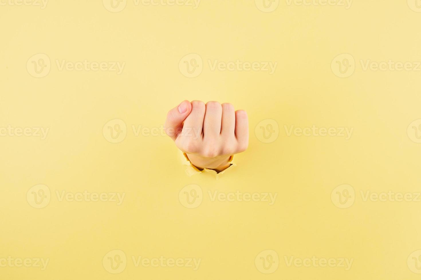 Woman showing her fist from the bursted hole on yellow cardboard background photo