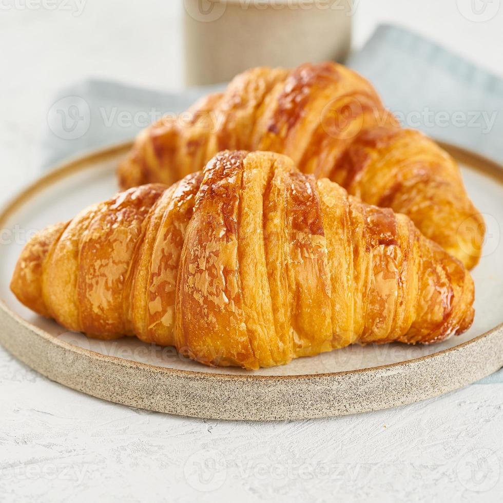 dos deliciosos croissants en plato y bebida caliente en taza. desayuno francés por la mañana foto