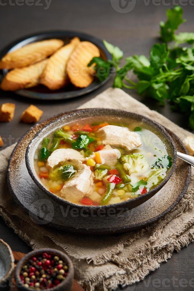 Homemade chicken soup with vegetables, broccoli on a dark brown background, photo