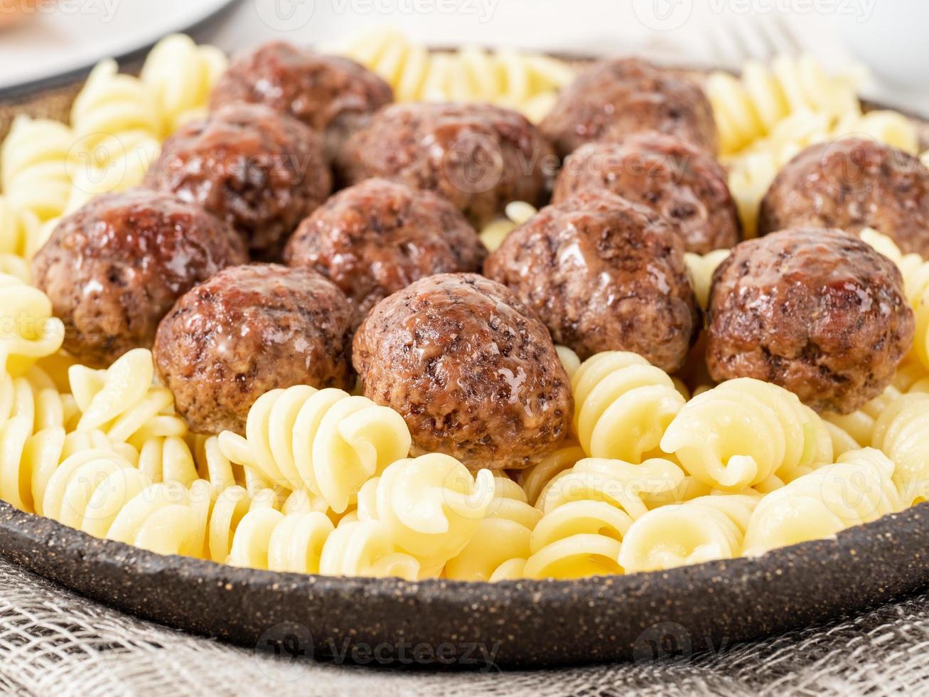 albóndigas suecas con pasta fusilli sobre mesa de madera blanca, vista lateral foto