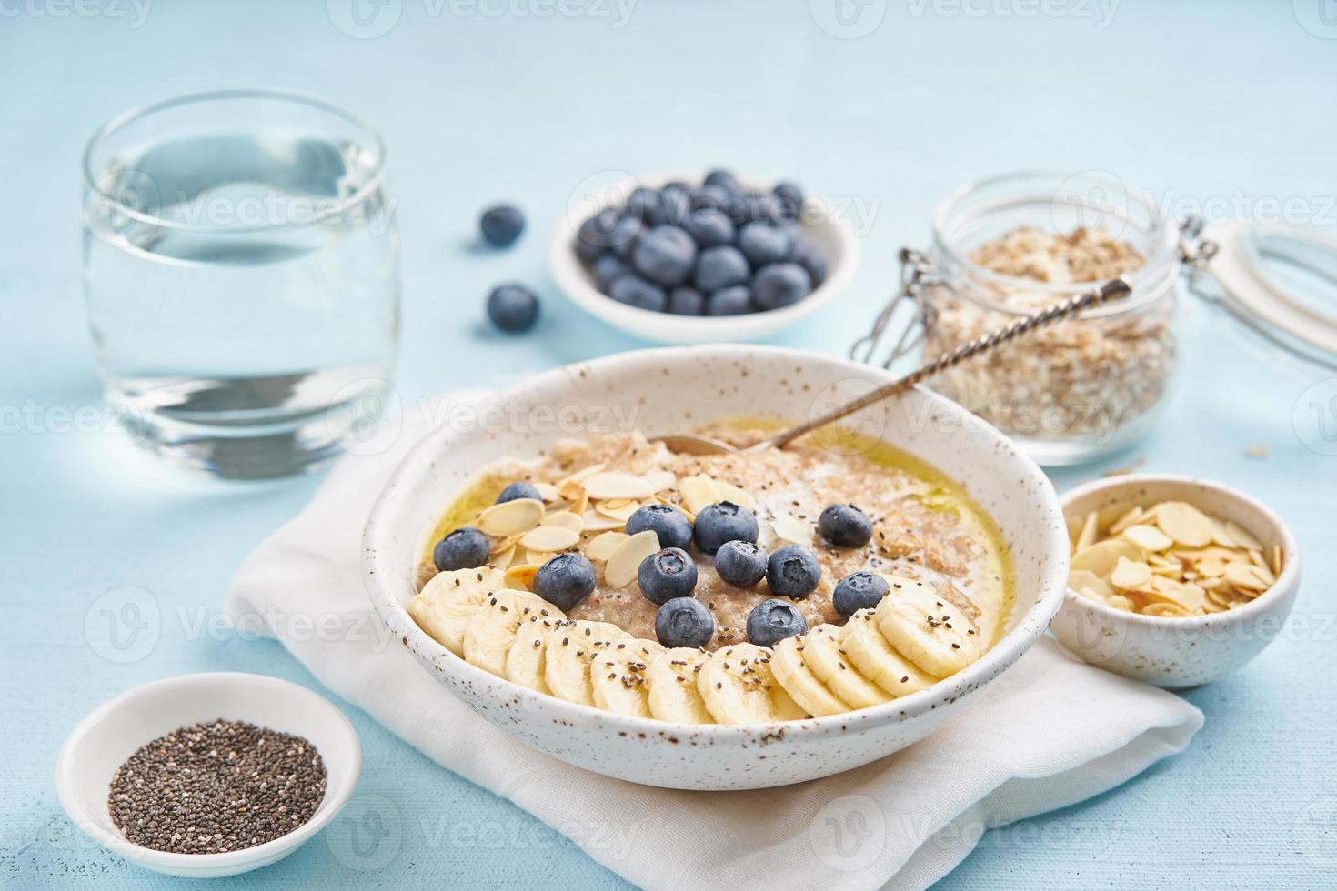 Oatmeal with blueberries, banana and cup of water on blue light background. photo