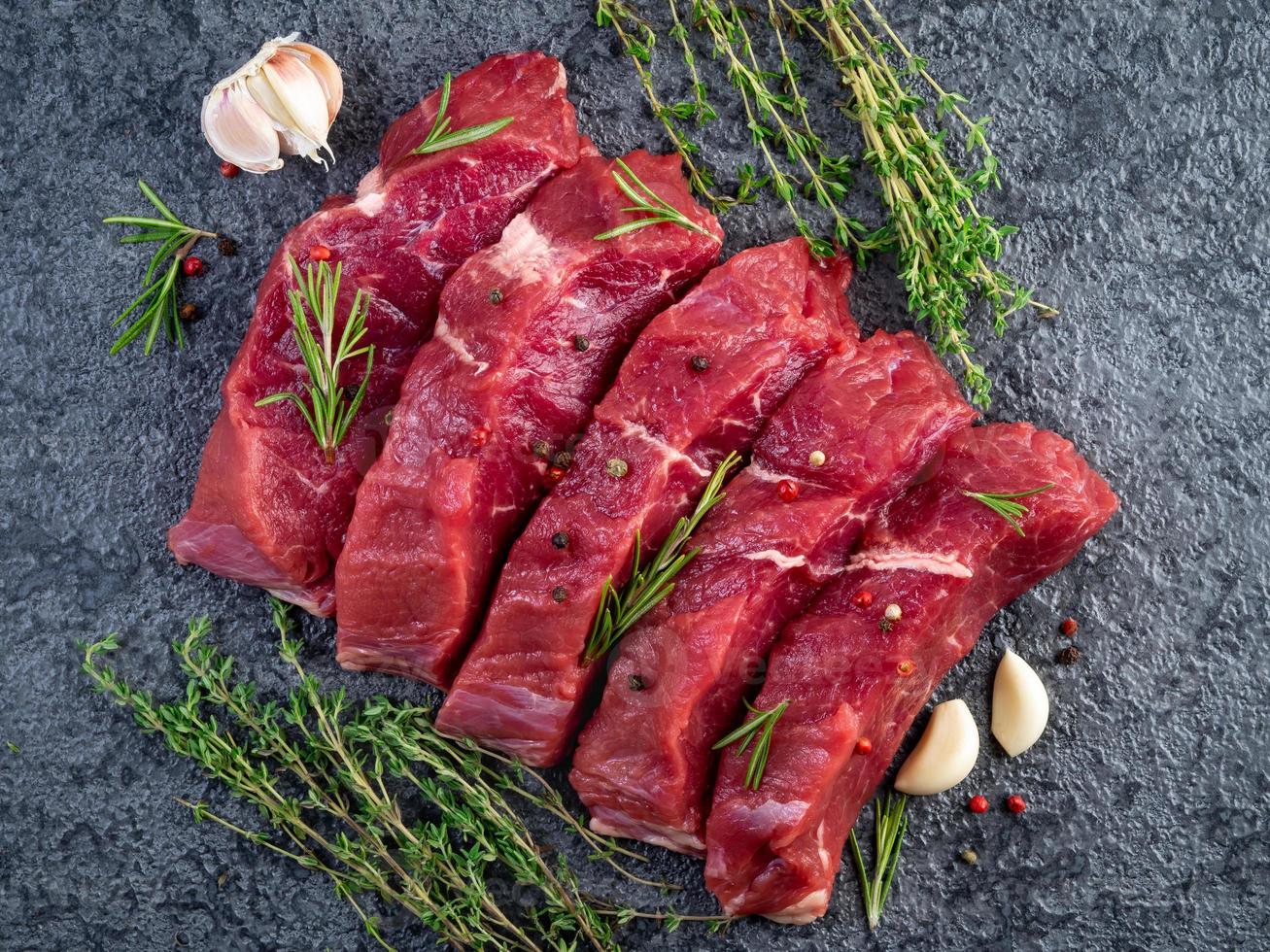 Raw meat, beef steak with seasoning on a black stone table, top view photo