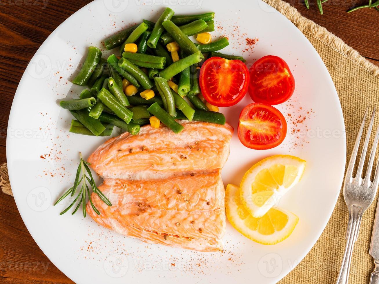 pescado salmón al vapor con verduras. comida de dieta saludable, telón de fondo de madera oscura foto