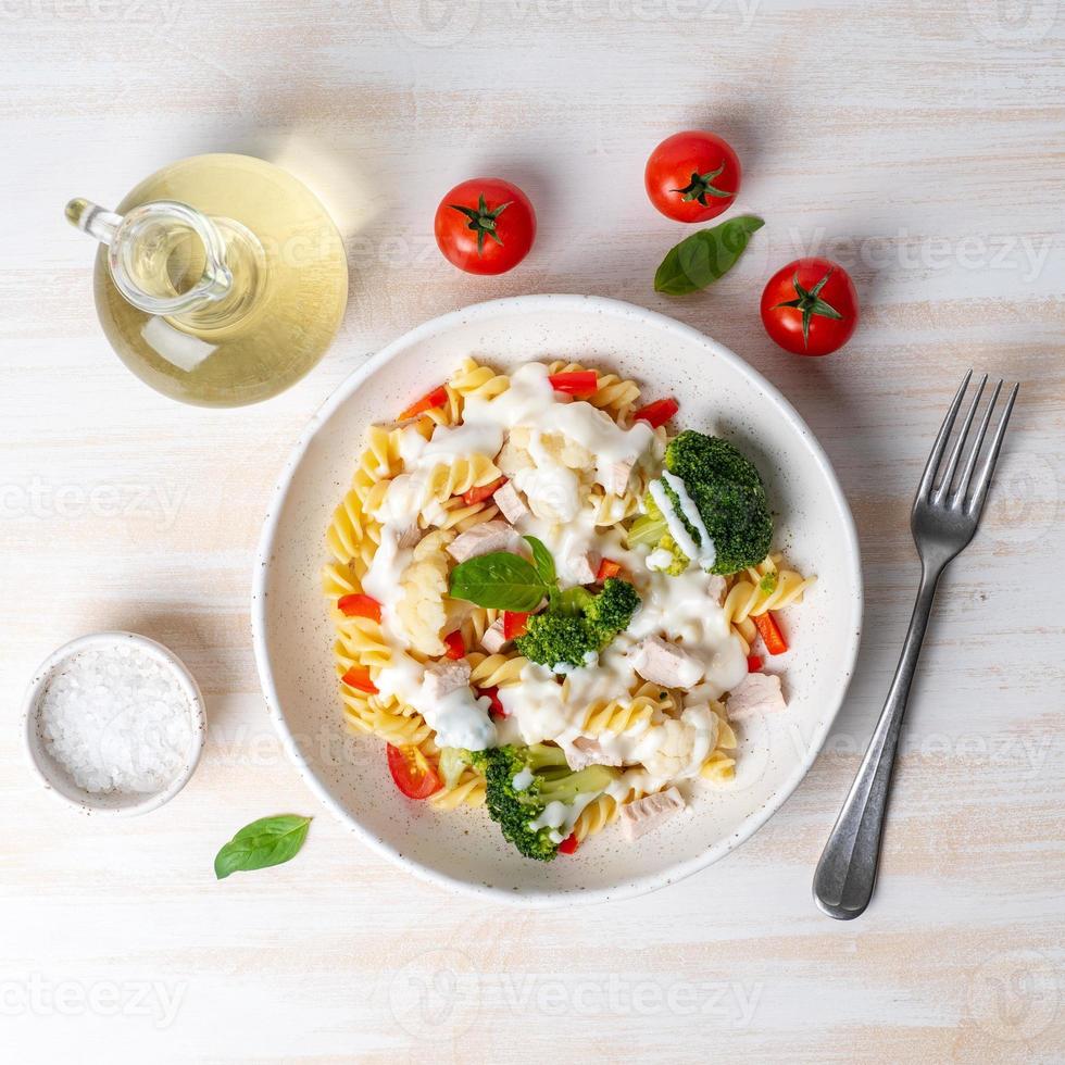 Pasta fusilli with vegetables, boiled steamed meat, white sauce on white wooden table photo