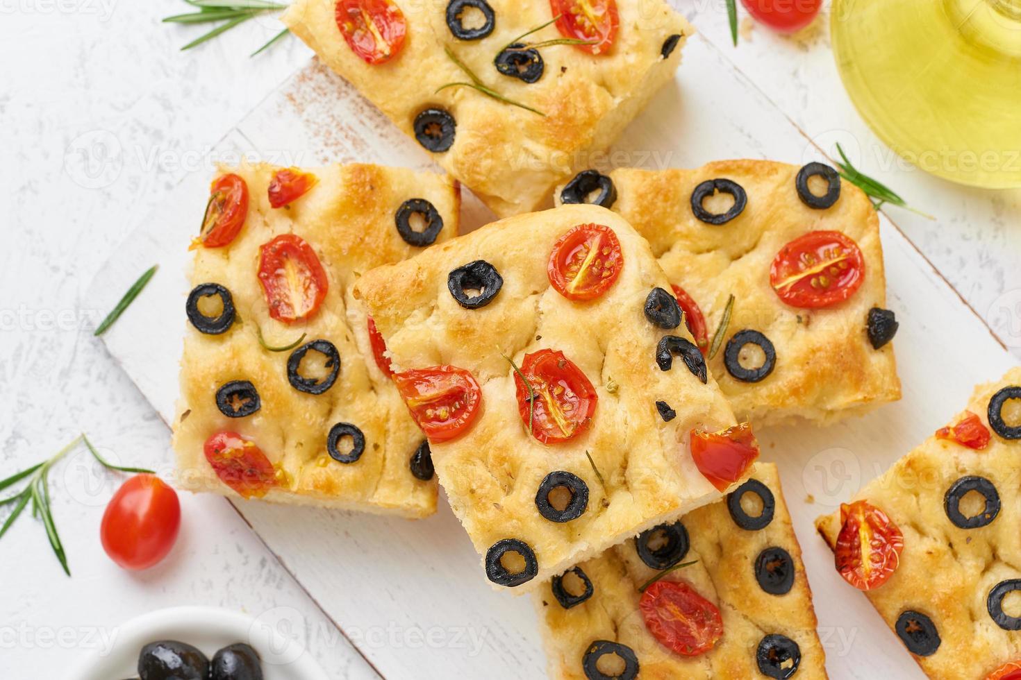 Sliced pieces of focaccia with tomatoes, olives and rosemary. Traditional Italian flat bread. photo