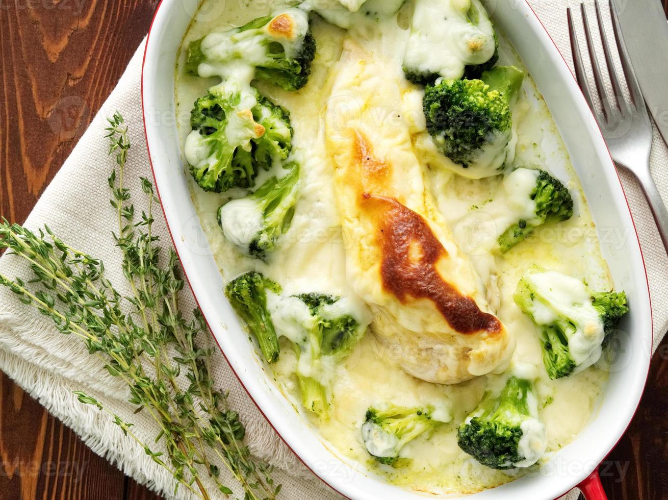 Chicken fillet baked with broccoli in bechamel sauce on dark wooden table. Healthy food photo