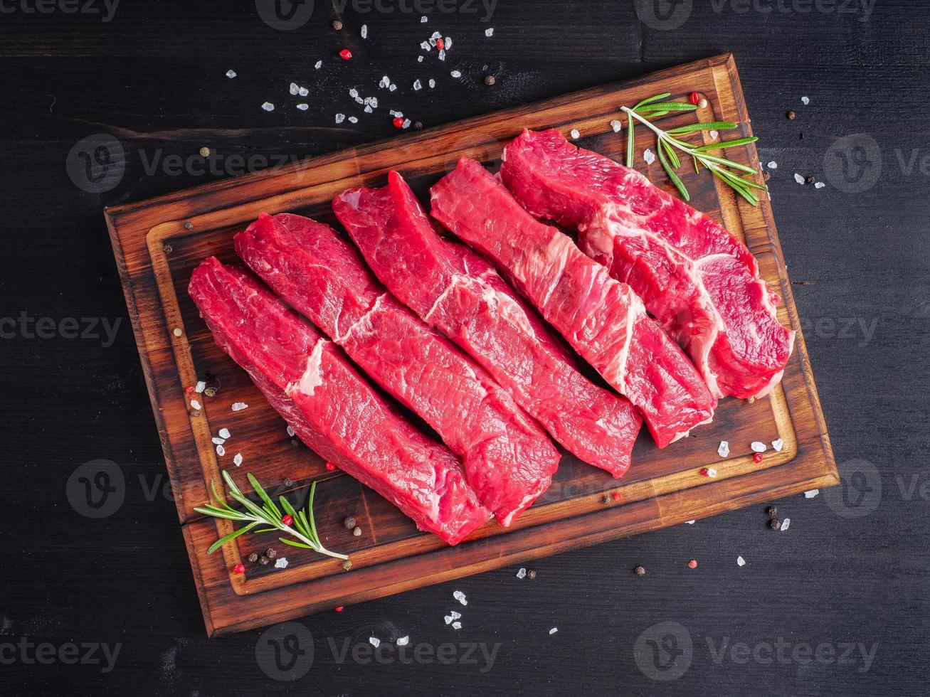 Raw meat, beef steak with seasoning on chopping board on dark background with rosemary, photo