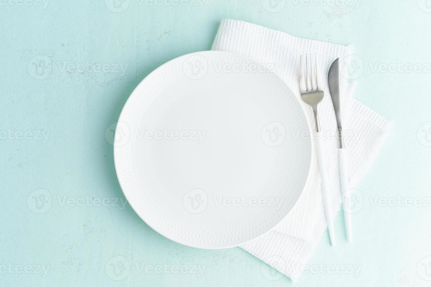 Clean empty white plate, fork and knife on green blue turquoise stone table, copy space, mock up photo