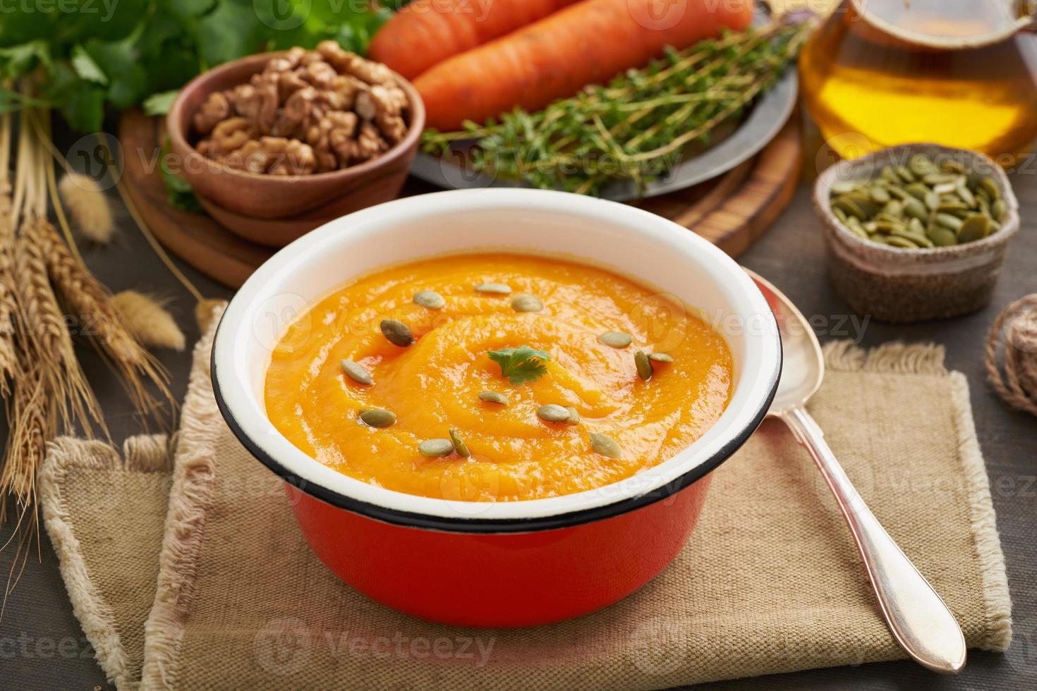 Pumpkin cream soup with seeds and walnuts, carrot, side view with autumn leaves for the atmosphere photo