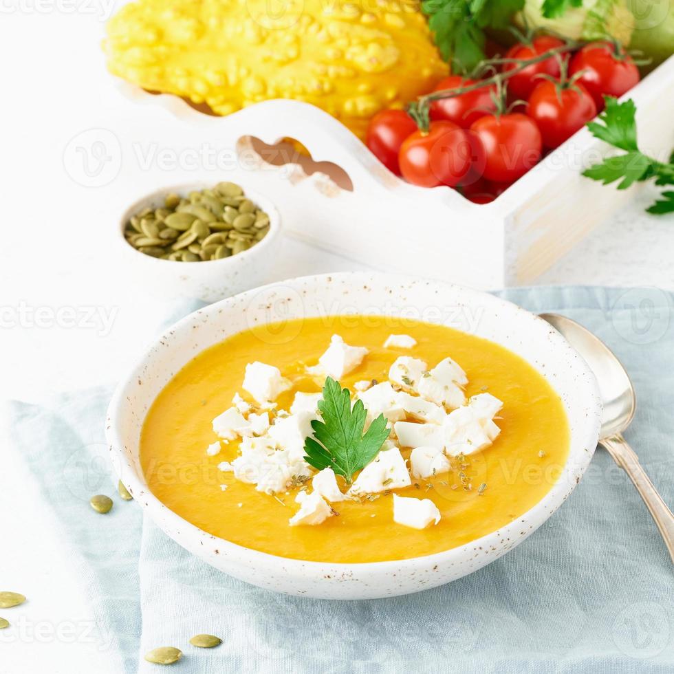 Pumpkin cream soup with feta cheese, autumn homemade food, white background, closeup photo