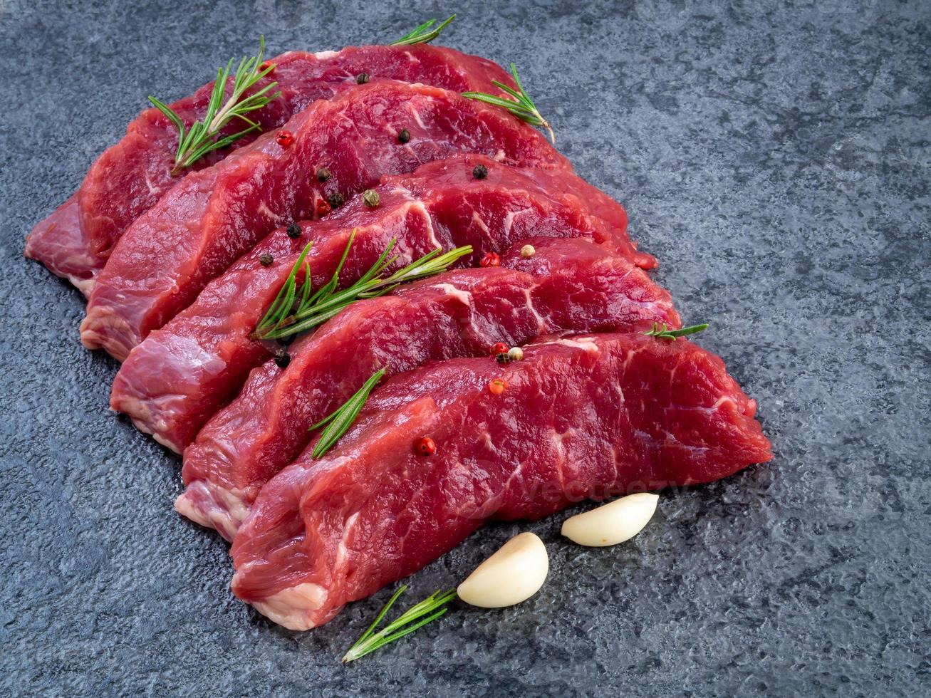 Raw meat, beef steak with seasoning on a black stone table, side view photo