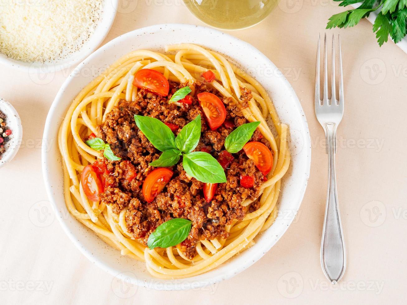 pasta bolognese with tomato sauce, ground minced beef, basil leaves on background photo