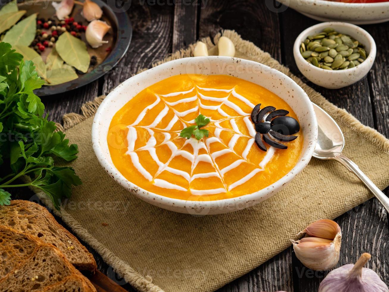 Funny food for Halloween. Pumpkin puree soup, spider web, dark old wooden table, side view. photo