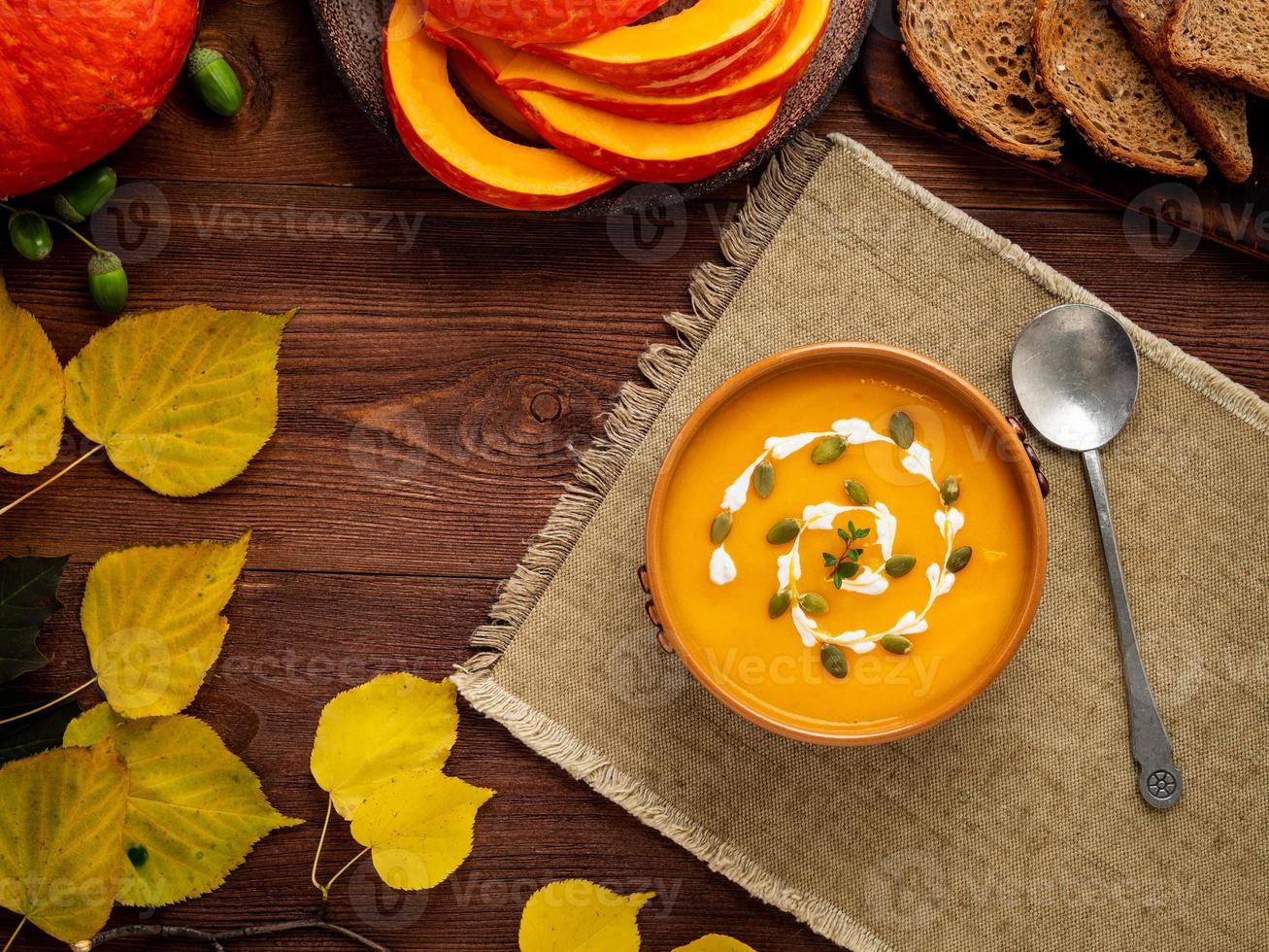 Autumn food. Pumpkin puree soup, leaves, dark brown old wooden table, top view, copy space photo