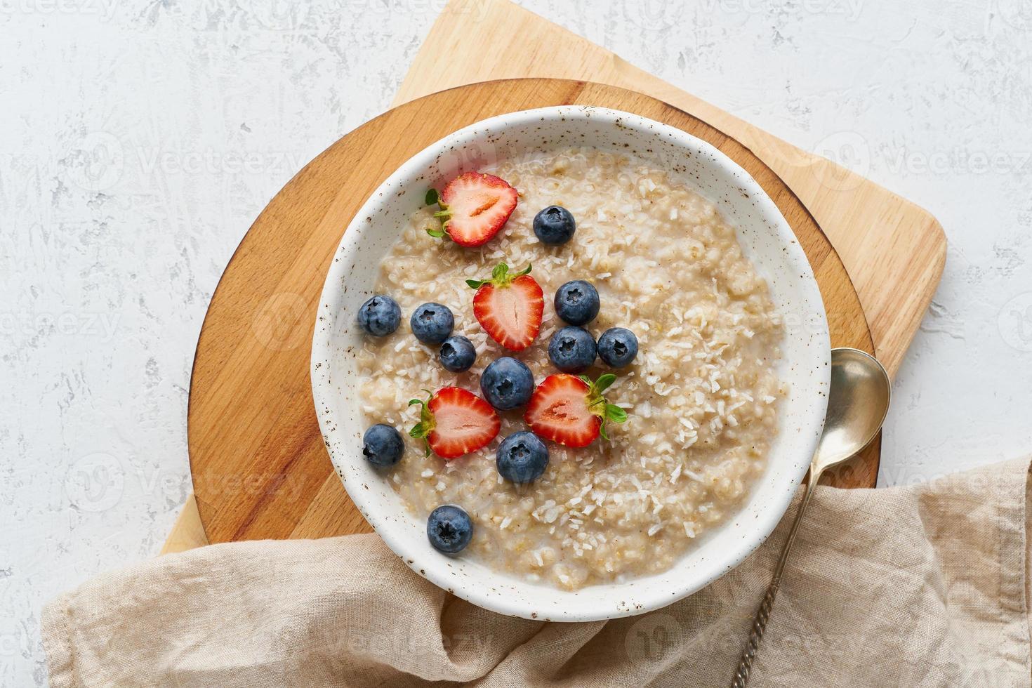 Oatmeal porridge rustic with berries, dash diet, on white wooden background top view photo