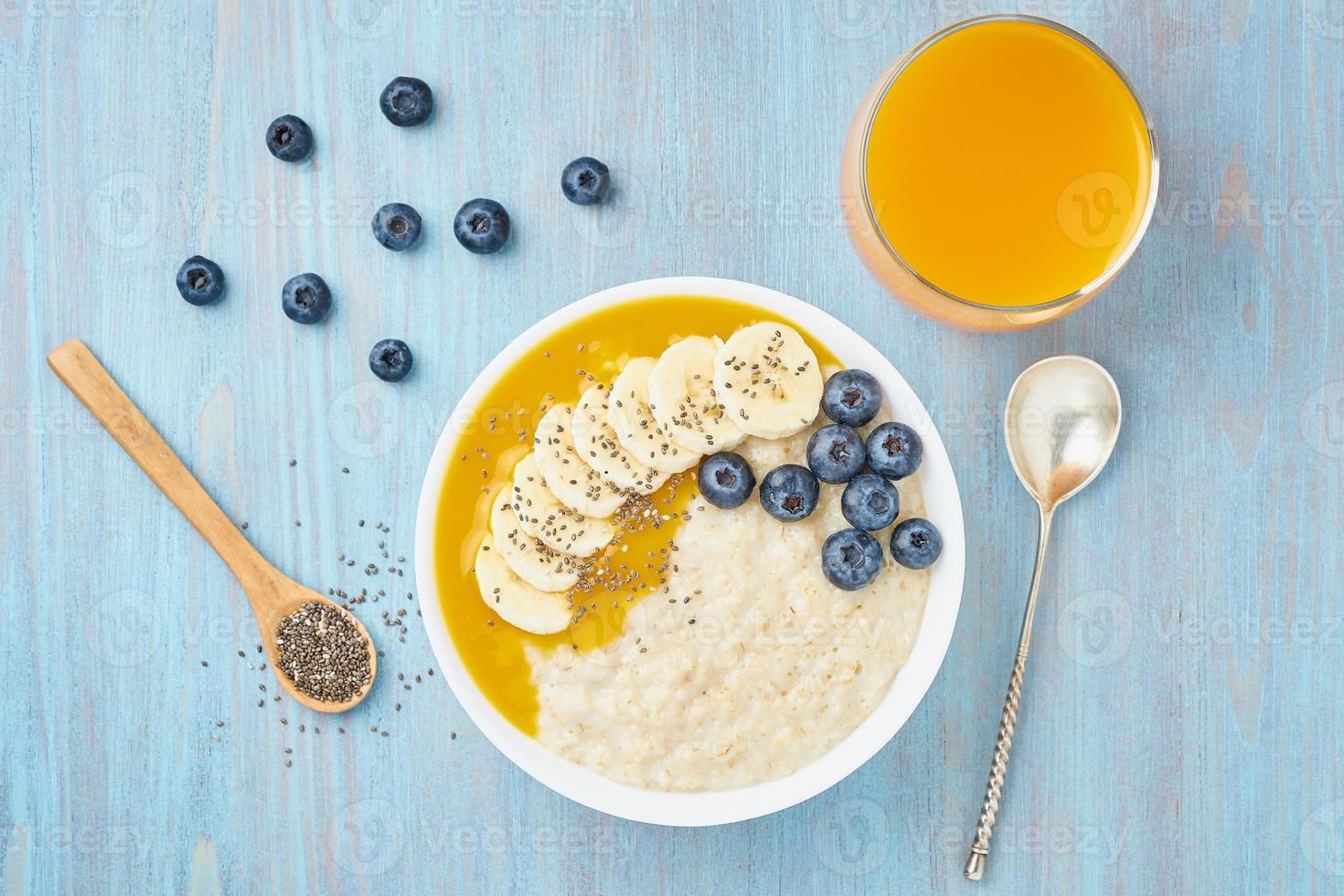 Oatmeal with bananas, blueberries, chia seeds, jam on blue wooden background. Top view. Healthy breakfast. photo