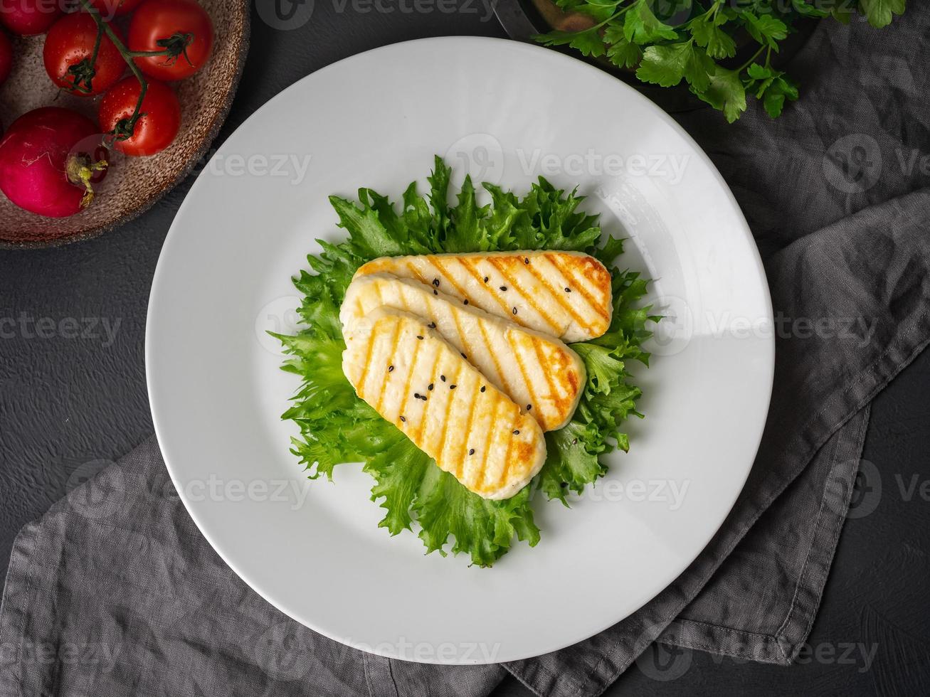 Grilled Halloumi, fried cheese with lettuce salad. Balanced diet, white plate on dark background, top view photo