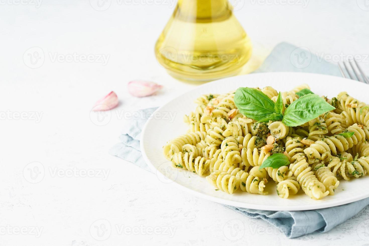 fusili pasta with basil pesto and herbs, italian cuisine, gray stone background, side view photo