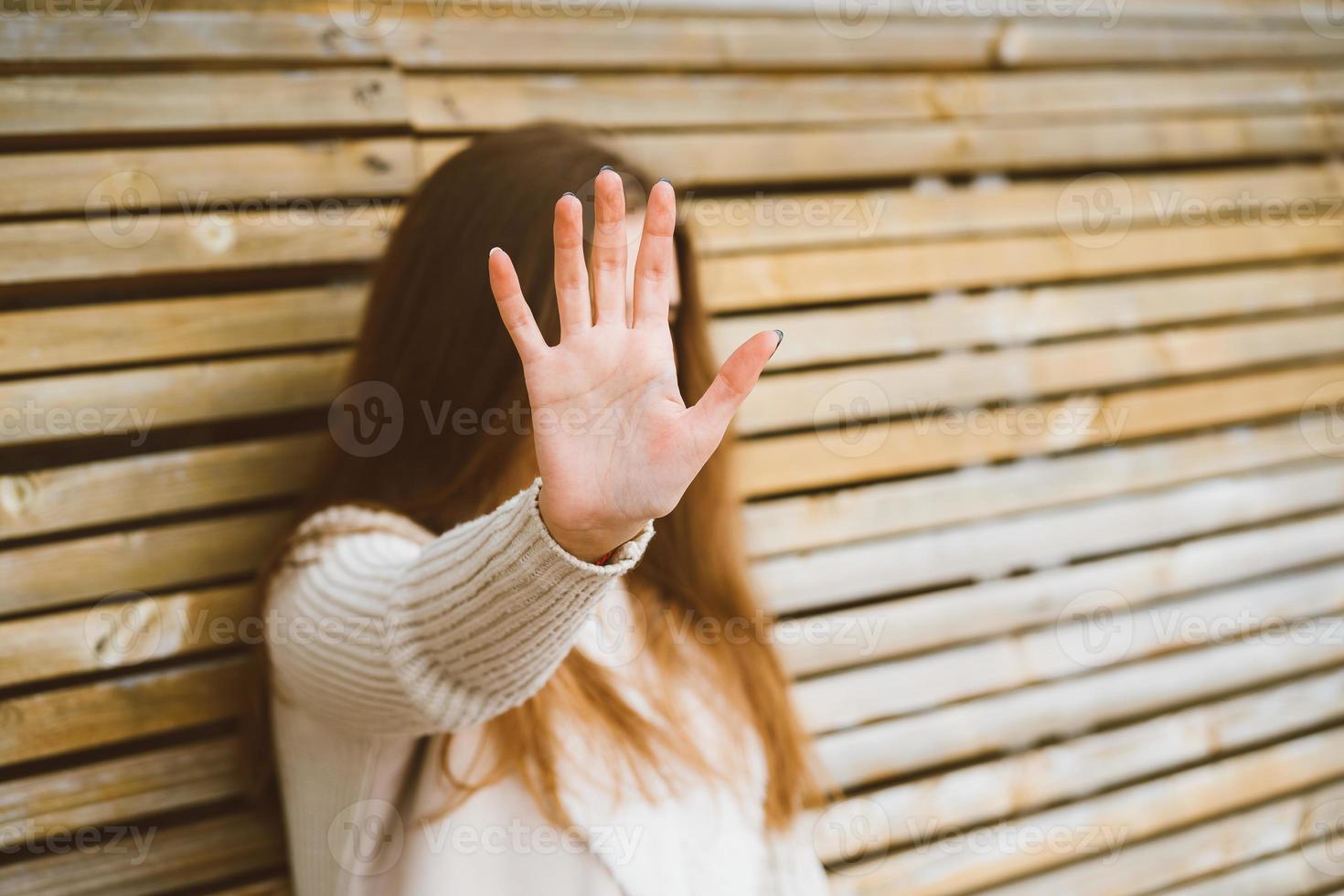 mujer con cabello largo se adelanta, protegiendo su rostro de la cámara. concepto de privacidad, espacio personal, prohibición de fotografía. una mujer se sienta en un banco de madera. para, hacer fotos está prohibido