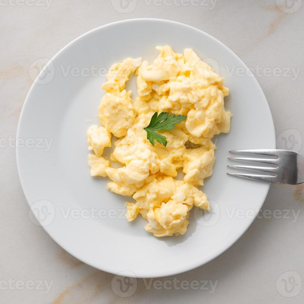white plate with pan-fried scrambled eggs on white light background with tomatoes. photo