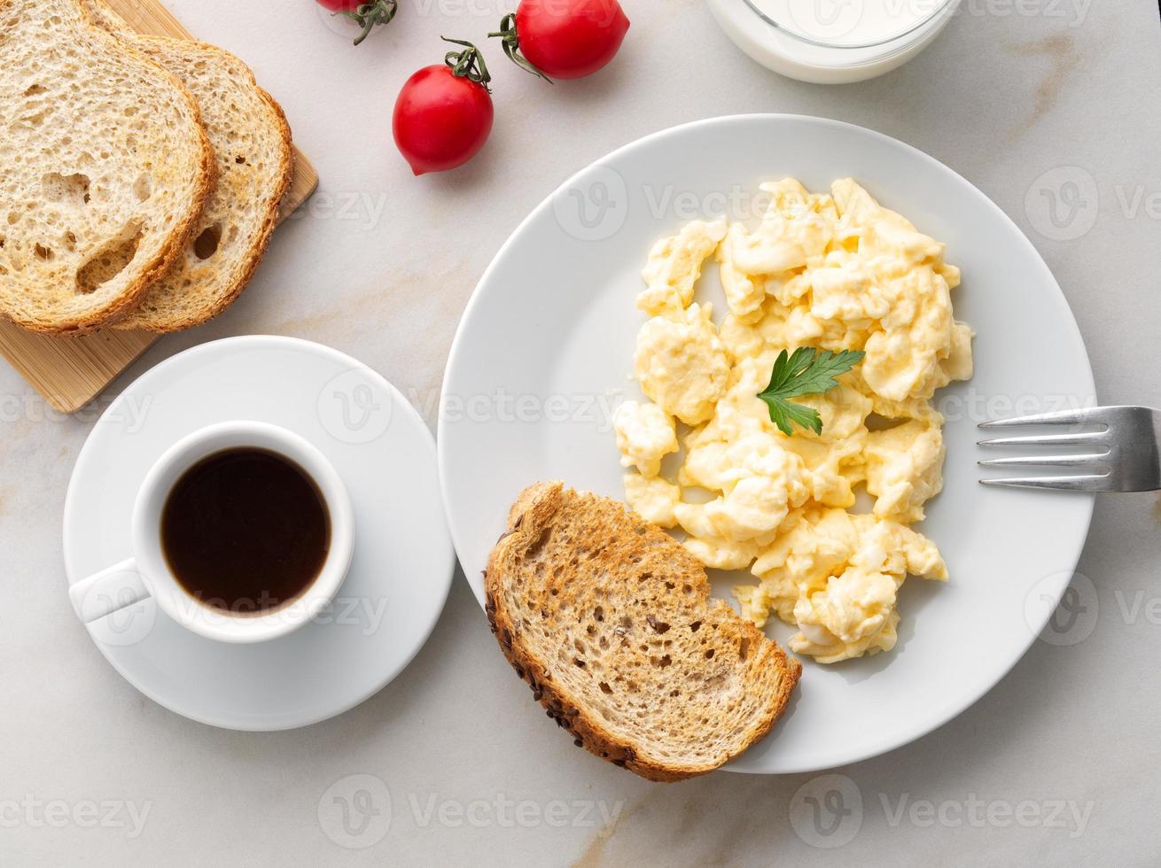 Breakfast with pan-fried scrambled eggs, cup of coffee, tomatoes on white stone background. photo