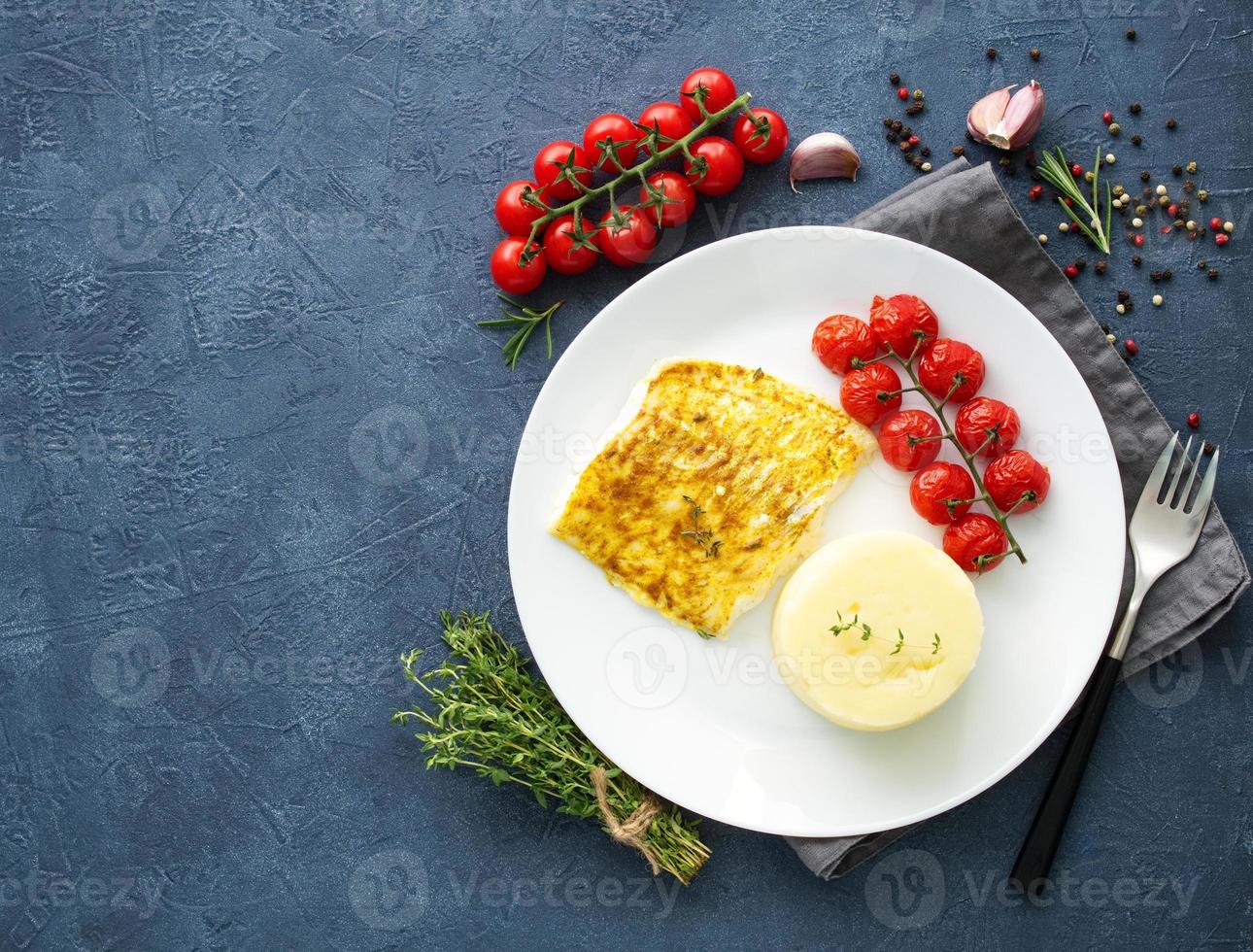 Fish cod baked in oven with mashed potatoes, tomatoes, diet healthy food. Dark gray background photo