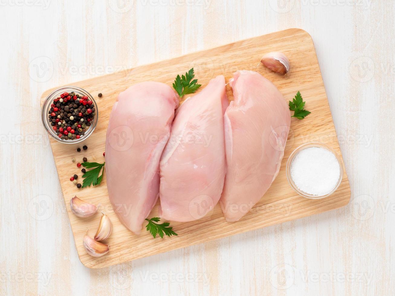 filete de pechuga de pollo crudo con especias en tablero de madera sobre mesa de madera blanca foto