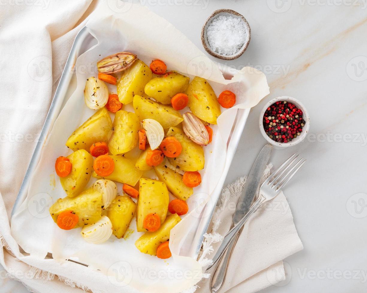 Colorful roasted vegetables on tray with parchment. Potatoes, carrots and onions. photo